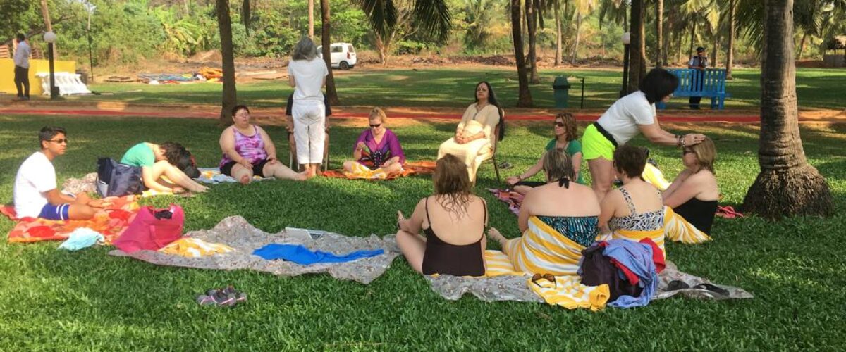 A group practising yoga on mats on the grass under palm trees
